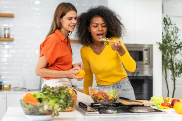 Wall Mural - Diversity young happy love LGBT, LGBTQ caucasian and african family lesbian couple woman cook vegan food healthy eat with fresh vegetable salad in kitchen at home, pride, rainbow.Lgbt lesbian couple