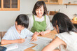 家で夏休みの宿題を手伝う母親と勉強する子供達
