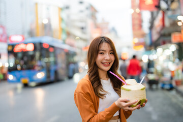 Young asian woman traveller standing and drinking coconut water. Beauty traveller female in city lifestyle chinatown street food market Bangkok, Thailand