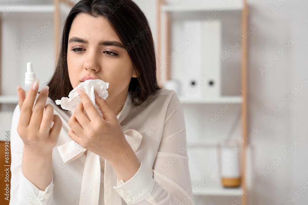 Sick woman with nasal drops in office