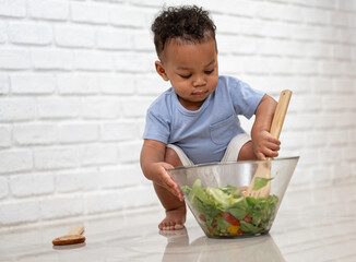 Baby or kid boy play cooking salad on floor at home