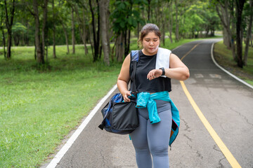 Wall Mural - Happy young overweight woman carring her exercise duffle bag and walking back after finishing her morning exercise run at a running track of a local park