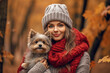 Beautiful young woman with knitted hat and scarf holding small dog in autumn forest