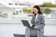 © Prostock-studio - Smiling Young Businesswoman Talking On Phone Websurfing On Laptop Outside