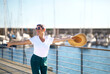 Cheerful Mature Woman Posing Holding Hat At Marina Dock Outdoor