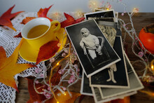 Old Vintage Monochrome Photographs Scattered On Rustic Wooden Table, Autumn Composition With Hot Tea In Mug, Fallen Yellow, Orange Leaves, Concept Family Tree, Genealogy, Cozy Autumn Mood