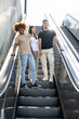 © carlesiturbe - Multiracial group of friends laughing and going down an outdoor escalator. Three happy young people smiling and looking relaxed walking down of stairs in the street.