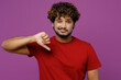 © ViDi Studio - Young dissatisfied displeased sad Indian man he wear red t-shirt casual clothes showing thumb down dislike gesture look camera isolated on plain purple background studio portrait. Lifestyle concept.