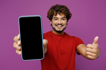 Wall Mural - Young Indian man he wear red t-shirt casual clothes hold in hand use close up mobile cell phone with blank screen workspace area show thumb up isolated on plain purple background. Lifestyle concept.