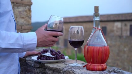 Wall Mural - Man testing red wine from the typical chianti wine bottle fiasco against the backdrop of the Tuscany landscape