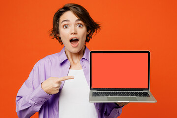 Wall Mural - Young fun IT woman she wear purple shirt white t-shirt casual clothes hold use work point on laptop pc computer with blank screen workspace area isolated on plain orange background. Lifestyle concept.