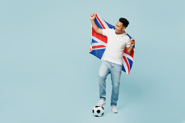 Wall Mural - Full body young happy fun man fan wear basic t-shirt cheer up support football sport team hold British flag soccer ball look aside watch tv live stream isolated on plain pastel blue color background.