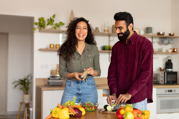 Excited young arab spouses cooking together, making delicious meal, talking and laughing, kitchen interior, copy space