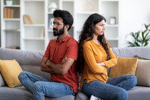Young Indian Couple Sitting Back To Back On Couch At Home