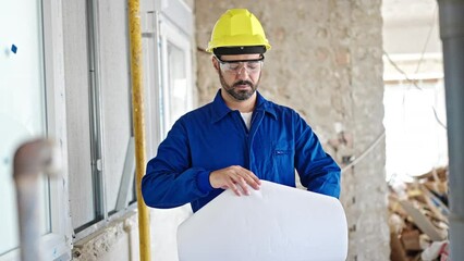 Wall Mural - Young hispanic man worker wearing hardhat holding blueprints at construction site