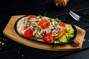 Sticker - Braised pieces of pork with onions, cream, tomatoes, lettuce, spices and herbs in a cast-iron skillet, dinner.