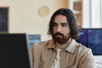 Young serious programmer looking at computer screen while analyzing data and creating new decoding algorithms by workplace in office