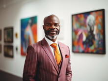 A Fictional Person, Not Based On A Real Person: Attractive Male African American Art Gallery Owner In Colorful Suit, Smiling And Looking At Camera While Posing In His Gallery With Colorful Paintings 