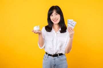 Poster - Portrait beautiful young business asian woman wearing white shirt and denim jean with a lot of cash money and piggy bank isolated on yellow background. Wealth money saving, finance investment concept.