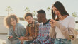 © Andrii Nekrasov - Happy group of friends using phone and smiling together outside. Students sit next to the university building looking at their mobile phones and talking