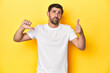 © Asier - Caucasian man in white t-shirt on yellow studio background showing thumbs up and thumbs down, difficult choose concept