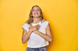 © Asier - Young blonde Caucasian woman in a white t-shirt on a yellow studio background, laughing keeping hands on heart, concept of happiness.