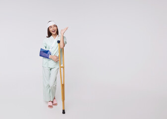 Asian woman wearing a patient gown put on a cast Use a crutch to walk due to accidental injury standing pointing to empty space with awesome smile insurance concept.