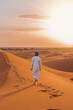 © ADDICTIVE STOCK - Anonymous Berber person walking on sand in desert