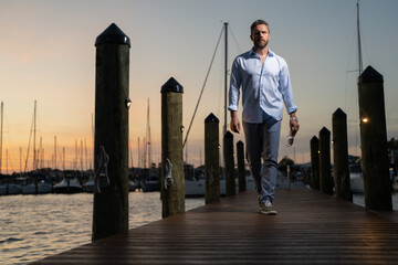 Rich summer business man near the yacht. Portrait of fashion male model outdoor. Rich male posing near yachts. Rich man in urban style. Rich man at yacht club. Man in gulf near luxury yacht ships.