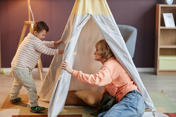 Wall Mural - Full length portrait of little boy with down syndrome playing with mother in play tent at home