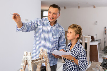 Wall Mural - Adult man and preteen boy holding documents and talking in new house, planning design projects