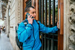 © ADDICTIVE STOCK - Male courier speaking on phone while calling client near entrance door