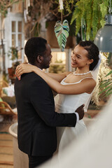 Vertical portrait of young black couple getting married and dancing together in room full of flowers and plants