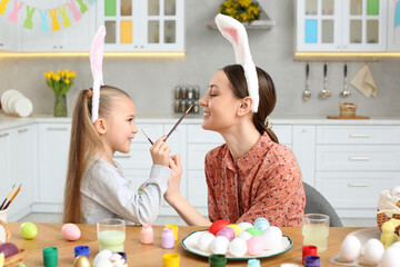 Wall Mural - Mother and her cute daughter having fun while painting Easter eggs at table in kitchen