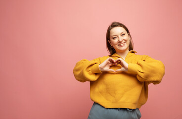 Adult woman smiling, showing hand heart gesture over chest and staring at camera, making love confession