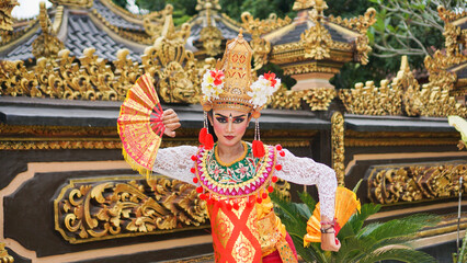 Wall Mural - girl wearing Balinese traditional dress with a dancing gesture on Balinese temple background with hand-held fan, crown, jewelry, and gold ornament accessories. Balinese dancer woman portrait
