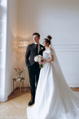 Wall Mural - The first meeting of the groom in a black suit and the bride in a white wedding dress with a bouquet in the interior of a photo studio on a white and black background