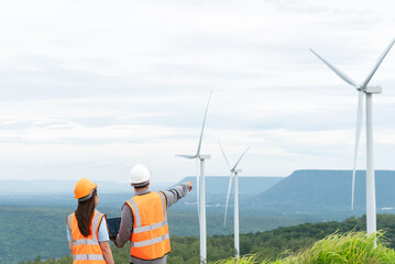 Wall Mural - Male and female engineers working on a wind farm atop a hill or mountain in the rural. Progressive ideal for the future production of renewable, sustainable energy.