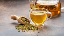 Herbal Infusion Fennel Tea In Glass Cup And Glass Tea Pot With Dried Fennel Seeds In Wooden Shovel. Herbal Tea Alternative Medicine Background Concept.