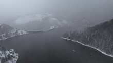 Aerial View Of A Lake And Dam Surrounded By A Captivating Blend Of Fog And Snow, Mountain Forest, In Dragan Dam From Transylvania, Romania