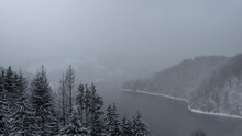 Aerial Panorama Of A Lake And Dam Surrounded By A Captivating Blend Of Fog And Snow, Mountain Forest, Aerial Lifting Up,in Dragan Dam From Transylvania, Romania