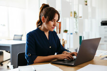 Businesswoman Working On Laptop At Desk In Creative Office