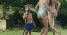 Slow Motion Portrait of Happy Children in Swimsuits Playing Together with Water and Having Fun in Garden. Little Toddler Boy Splashing his Sisters Playfully as They Run. Concept of Childhood Games