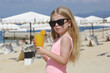 Adorable little girl having fresh squeezed orange juice in a beach bar, hydratation and healhy diet during hot summer days
