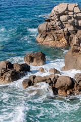 Waves on rocky beach, sea shore with waves crushing over the big rocks, summer sunny day