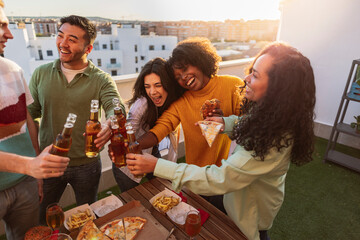 group of diverse friends partying on rooftop drinking alcohol and eating, toasting with beers