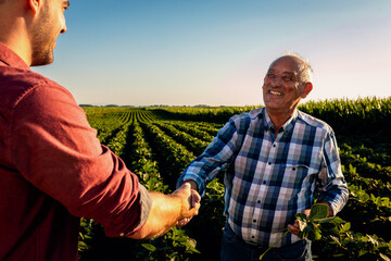 Two farmers in soy field making agreement with handshake at sunset.