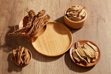 A wooden plate in round-shaped with several plates of Bai Zhu and Angelica root displayed around. Blank space for medicine product presentation