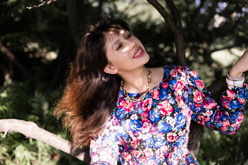 young brunette female standing under tree leaves in urban park at spring or summer day