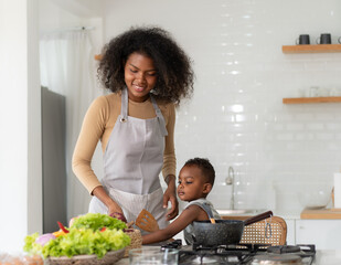 Wall Mural - Multiracial mother and son have fun cooking meal together in kitchen at home. Young multiethnic woman and her little child preparing healthy lunch with fresh vegetable. Happy motherhood lifestyle.
